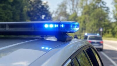Blaues Blaulicht leuchtet auf dem Dach eines Polizeifahrzeugs mit einem weiteren Streifenwagen im Hintergrund