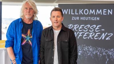 Zwei Männer stehen vor einem Banner mit der Aufschrift Willkommen zur heutigen Presse-Konferenz.