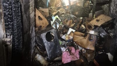 Blick durch eine Tür in einen verrauchten und stark verkohlten Keller voller Brandtrümmer.