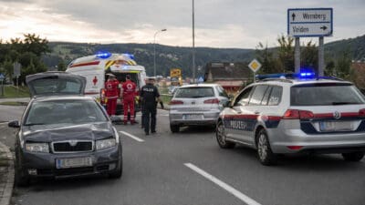 Ein beschädigtes graues Auto steht neben einem Polizeiwagen und einem Rettungswagen an der Unfallstelle.