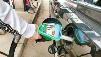 Eine Hand führt eine grüne Zapfpistole in den Einfüllstutzen eines Autos an einer Tankstelle.