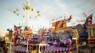 Bunt beleuchtetes Break Dance Karussell mit drehenden Gondeln neben einem hohen Kettenkarussell auf dem Jahrmarkt.
