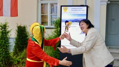 Ein in Rot und Gelb gekleideter Clown und eine Frau vor einem digitalen Display in Gerasdorf.