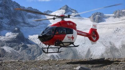 Roter und weißer Rettungshubschrauber fliegt vor schneebedeckten Bergen und Gletscher.