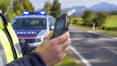 Polizist haelt Atemalkoholtestgeraet in der Hand vor Polizeiwagen mit Blaulicht