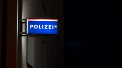 Beleuchtetes blaues Polizeischild mit der Aufschrift POLIZEI an einer Wand bei Nacht