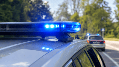Nahaufnahme eines blauen Blaulichts auf dem Dach eines Polizeifahrzeugs mit einem weiteren Einsatzwagen im Hintergrund.