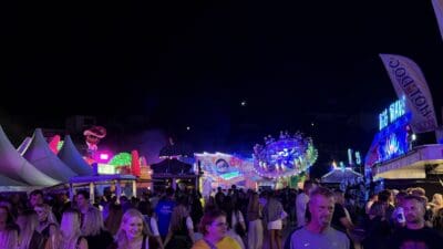 Menschenmenge auf dem nächtlichen Bleiburger Wiesenmarkt vor bunten beleuchteten Fahrgeschäften und Ständen
