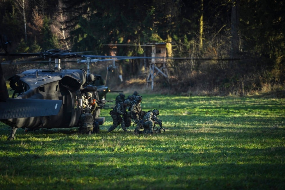 Soldaten in Tarnuniform steigen aus einem Hubschrauber auf einer Wiese aus