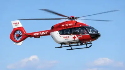 Rot-weißer Notarzthubschrauber der Flugrettung fliegt vor blauem Himmel.