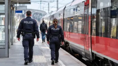 Polizeikräfte gehen auf einem Bahnsteig neben einem roten Zug.