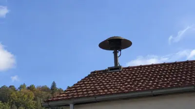 Eine Sirene steht auf dem Ziegeldach eines Hauses vor blauem Himmel.