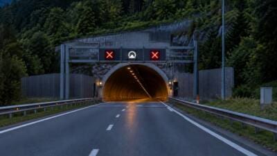 Eine Straße führt bei Dunkelheit auf einen Tunnel mit leuchtenden roten X-Anzeigen zu.