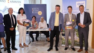 Gruppe von Personen bei einer Pressekonferenz vor Bannern der Welt Kärntner in Klagenfurt