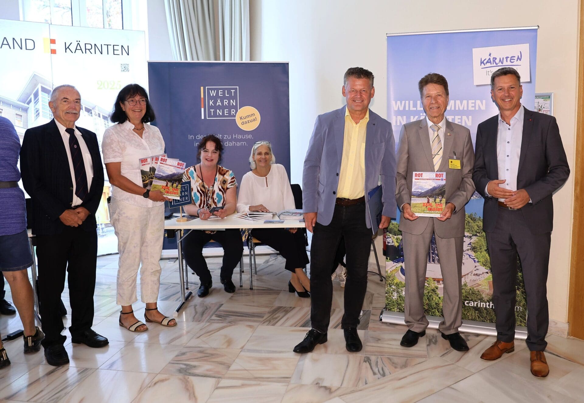 Gruppe von Personen bei einer Pressekonferenz vor Bannern der Welt Kärntner in Klagenfurt