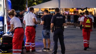 Sanitäter des Roten Kreuzes und ein Polizist betreuen einen verletzten jungen Mann vor einem Festzelt.