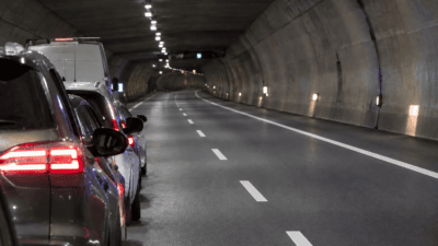 Mehrere Autos mit roten Rücklichtern stehen hintereinander in einem beleuchteten Autobahntunnel.