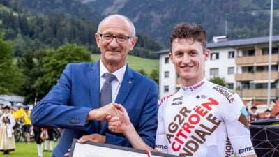 Anton Mattle und Felix Gall schütteln sich die Hände und halten ein gerahmtes Bild vor Berglandschaft.