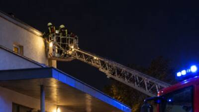 Feuerwehrleute in einem Korb einer Drehleiter an der Dachkante eines Gebäudes bei Nacht