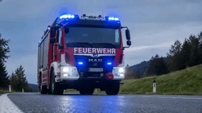 KI-generiertes Bild: Rotes Feuerwehrfahrzeug mit blauem Blaulicht auf einer Landstraße bei Dämmerung