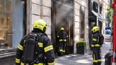 Feuerwehrleute mit Atemschutzgeräten vor dem rauchenden Eingang einer Prada Boutique