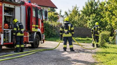 Feuerwehrleute in Schutzkleidung mit Atemschutzgeräten stehen bei einem Löschfahrzeug und halten gelbe Schläuche