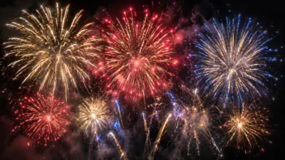 Bunte Feuerwerksfontänen in Gold, Rot und Blau erhellen einen dunklen Nachthimmel.