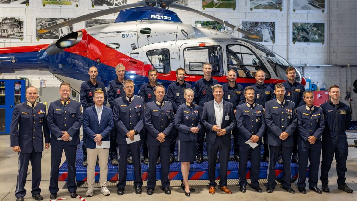 Gruppe von Polizisten in Uniform und einem Mann in Anzug vor einem Hubschrauber in einer Halle