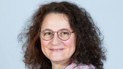 Porträt einer Frau mit lockigem dunklem Haar, runder Brille und gemustertem Schal