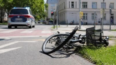 Ein umgestürztes Fahrrad liegt am Straßenrand vor einem Polizeiwagen mit Blaulicht.
