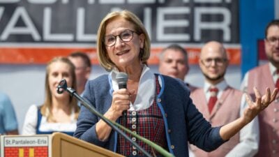 Eine Frau mit Brille und Tracht spricht in ein Mikrofon am Rednerpult.