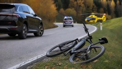 Umgestürztes E-Bike liegt am Straßenrand neben Polizeiwagen und Rettungshubschrauber.