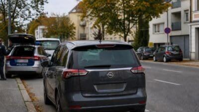 Ein grauer Opel Kombi parkt auf einer herbstlichen Straße neben einem Polizeiauto.