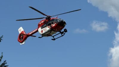 Roter und weißer Rettungshubschrauber mit laufendem Rotor vor blauem Himmel