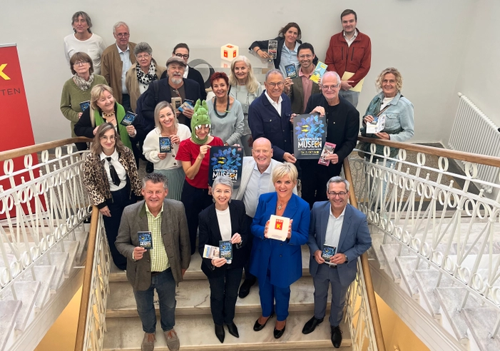 Gruppe von Menschen auf einer Treppe hält Broschüren mit der Aufschrift Museen in den Händen.