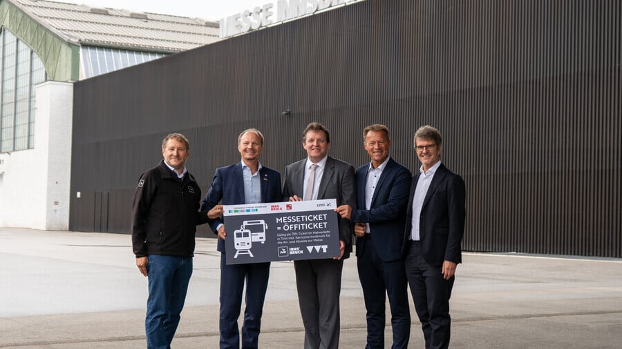 Fünf Männer präsentieren vor dem Messegebäude ein Schild zum Messeticket als Öffi-Ticket.