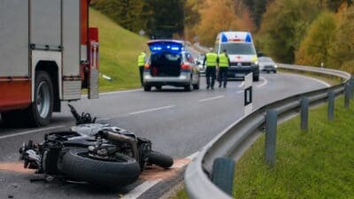 Verunglücktes Motorrad liegt vor Einsatzfahrzeugen mit Blaulicht an einer Landstraße im Herbst.