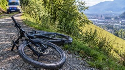 Ein umgestürztes Mountainbike liegt auf einem Schotterweg mit einem Rettungswagen im Hintergrund.