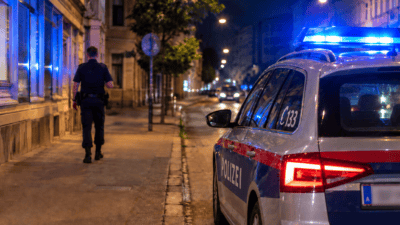 Polizeiwagen mit Blaulicht auf nächtlicher Straße und Polizist zu Fuß unterwegs
