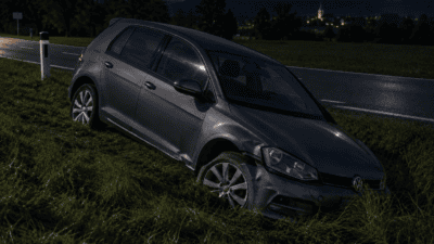 Ein beschädigter grauer Volkswagen liegt im Straßengraben neben einer Landstraße bei Nacht.