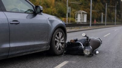 Ein graues Auto kollidiert mit einem umgestürzten Roller auf einer nassen Straße
