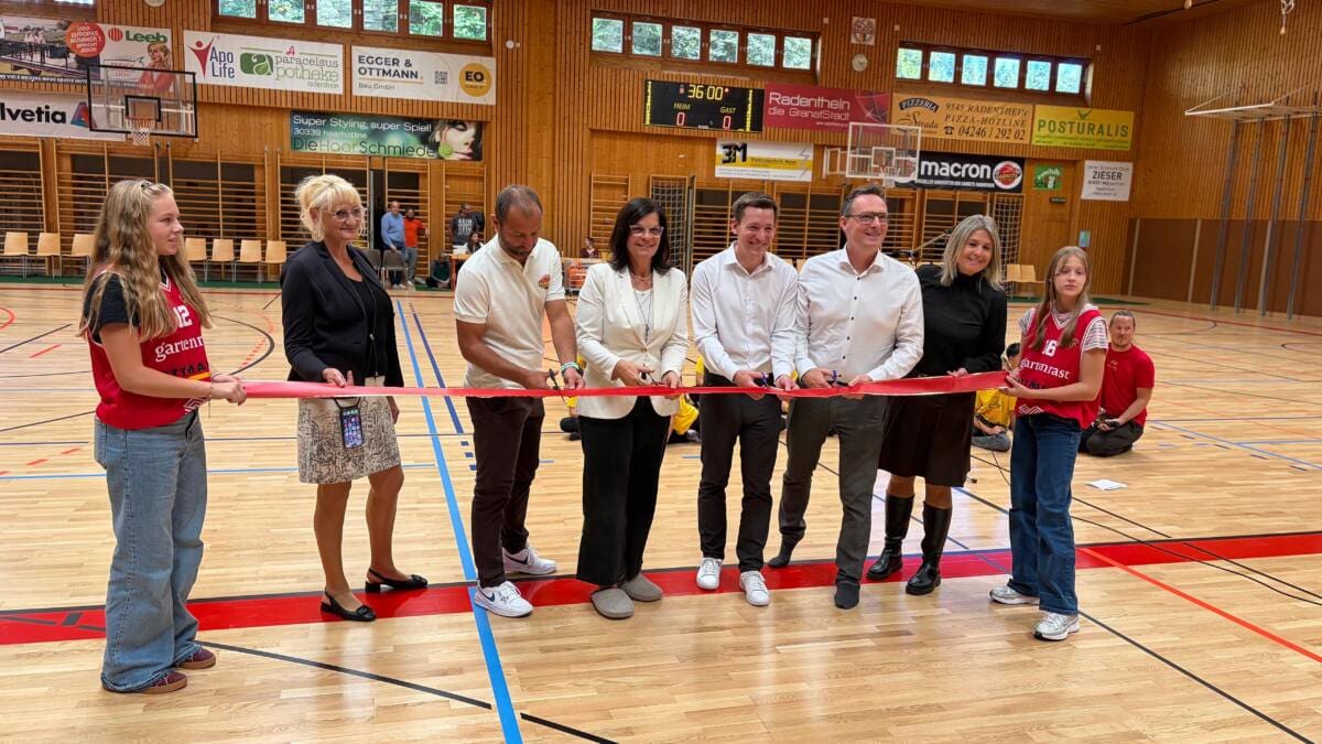 Menschen durchtrennen ein rotes Band auf dem neuen Sporthallenboden in Radenthein