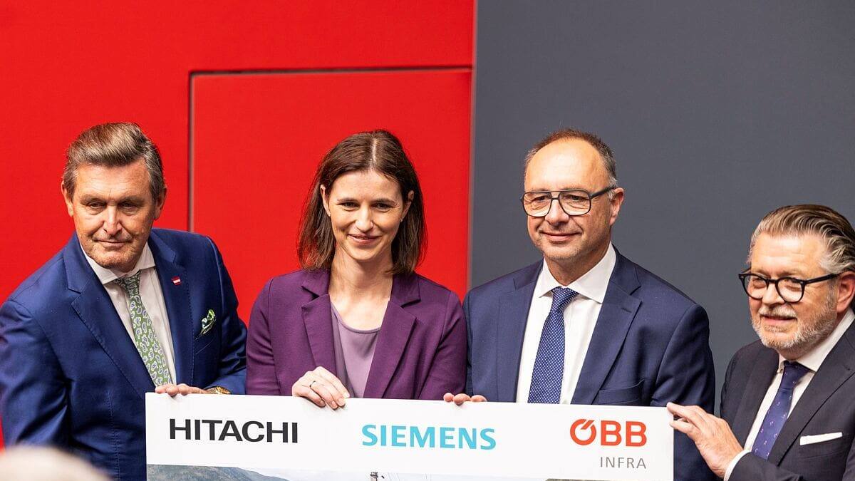 Personen in Anzügen präsentieren ein großes Schild mit den Logos von Hitachi, Siemens und ÖBB zu digitalen Stellwerken in Österreich.