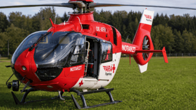 Ein roter und weißer Notarzthubschrauber der ARA Flugrettung steht auf einer grünen Wiese