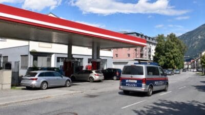 Österreichischer Polizeiwagen steht auf der Straße vor einer Tankstelle mit rotem Dach und parkenden Autos
