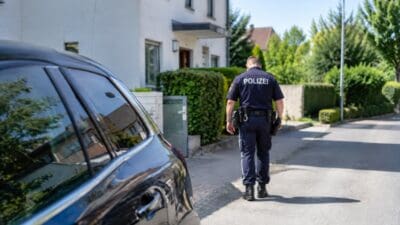 Ein Polizist in Uniform geht auf ruhiger Vorstadtstraße an schwarzem Auto vorbei