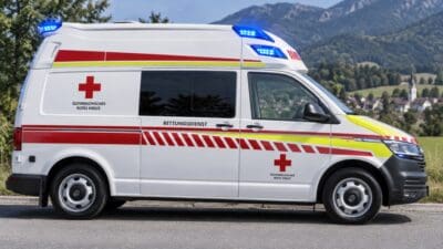 Weißer Rettungswagen des Österreichischen Roten Kreuzes mit Blaulicht und roten Warnstreifen vor Berglandschaft