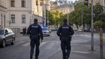 Zwei Polizisten laufen über eine Kreuzung, im Hintergrund ein Streifenwagen mit Blaulicht