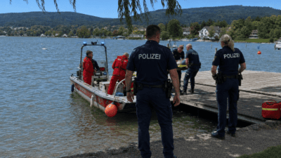 Polizisten und Rettungskräfte stehen mit einem Boot an einem Steg am Seeufer