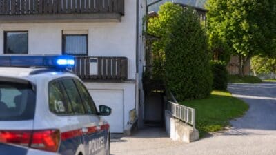 Weißes Polizeiauto mit blauem Blaulicht vor einem weißen Wohnhaus mit Balkon in den Bergen